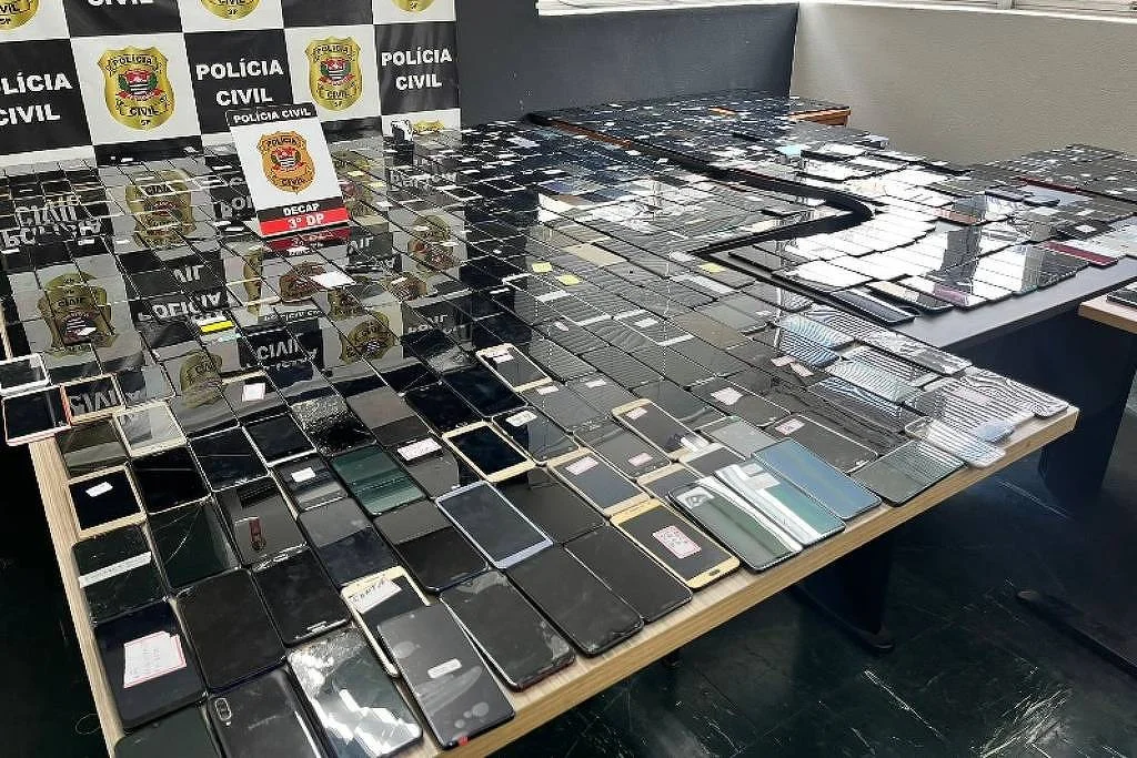 diversos celulares roubados em cima da mesa com o logo da polícia civil atrás